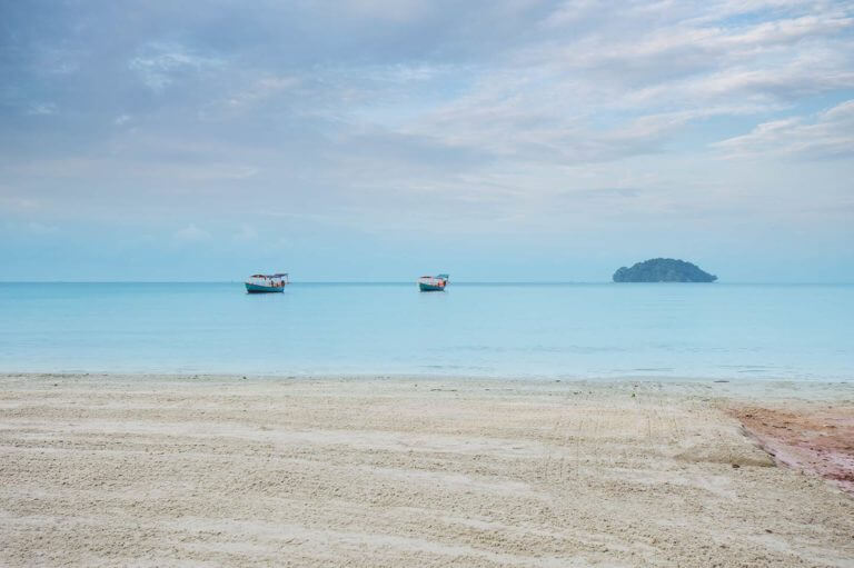 Blick auf das Meer mit zwei Fischerbooten und einer Insel am Otres Beach in Sihanoukville in Kambodscha