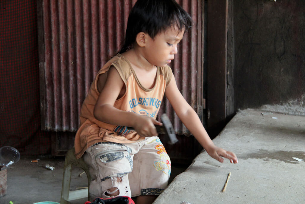 Cambodia: Child playing with a hammer