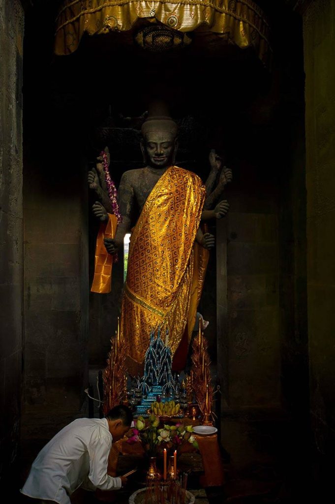 Holy Vishnu statue near the Gopuram at Angkor Wat. A person brings gifts and knees in front of the statue. 