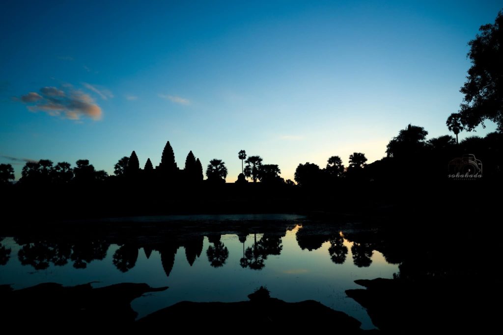 Sunrise at Angkor Wat with a small cloud and water reflection.